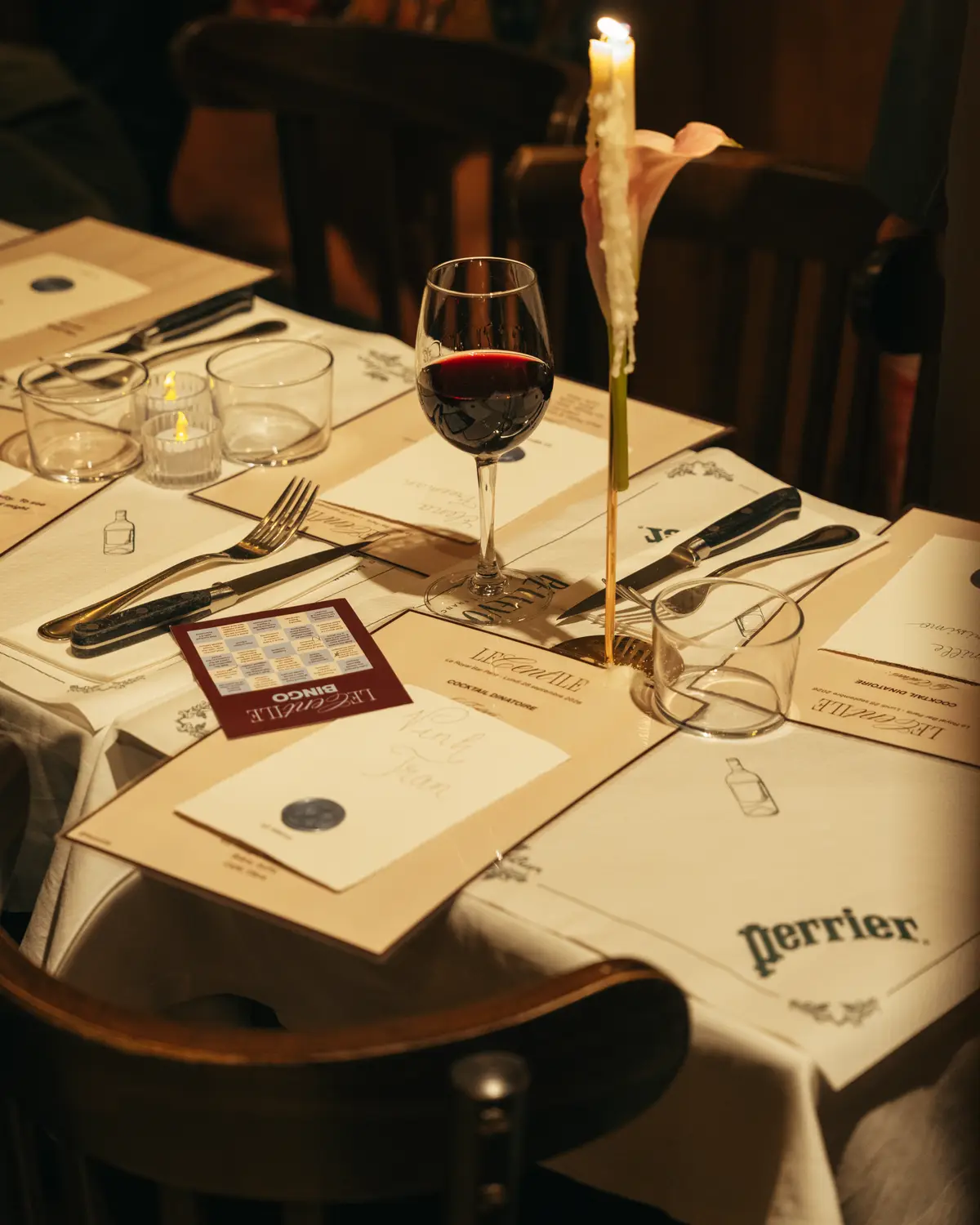A place set with a menu, a candle and a glass of red wine