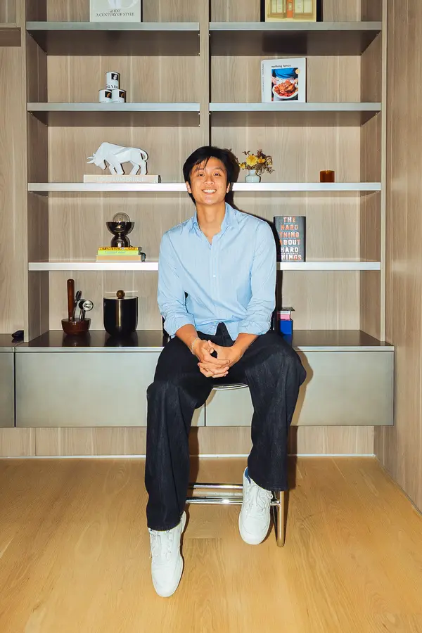 A guest smiling on a stool in front of a bookcase